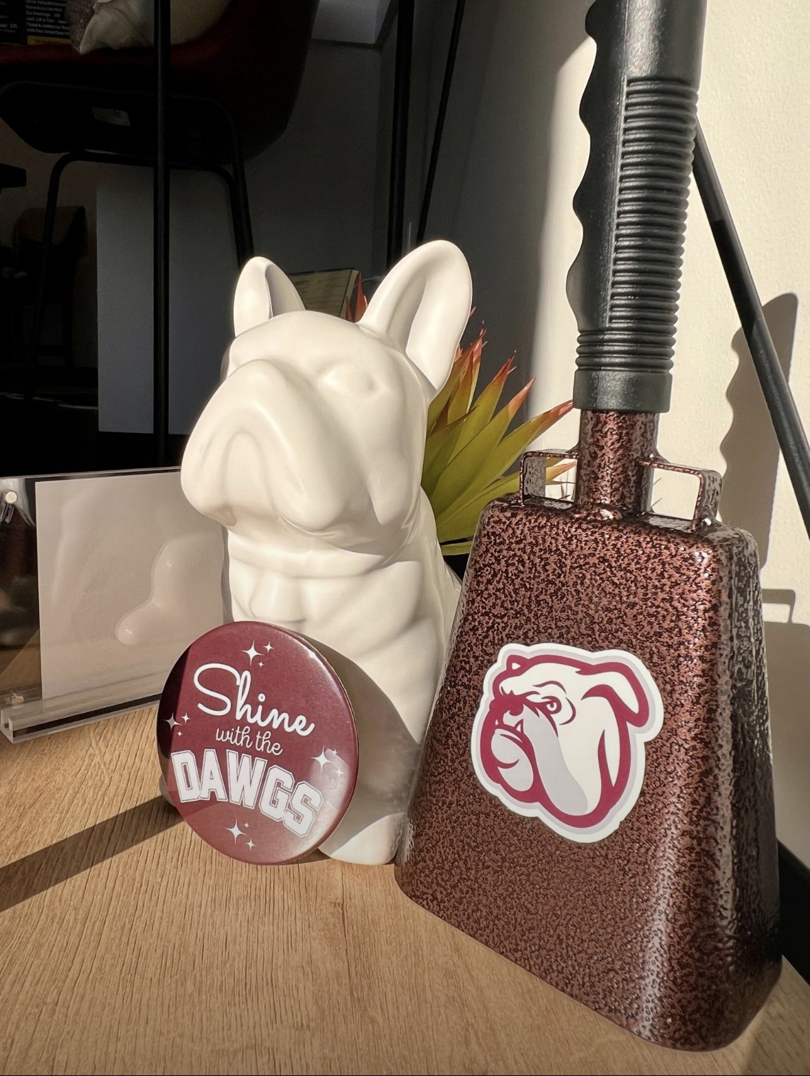 A Shine with the Dawgs button beside a ceramic bulldog and a maroon cowbell